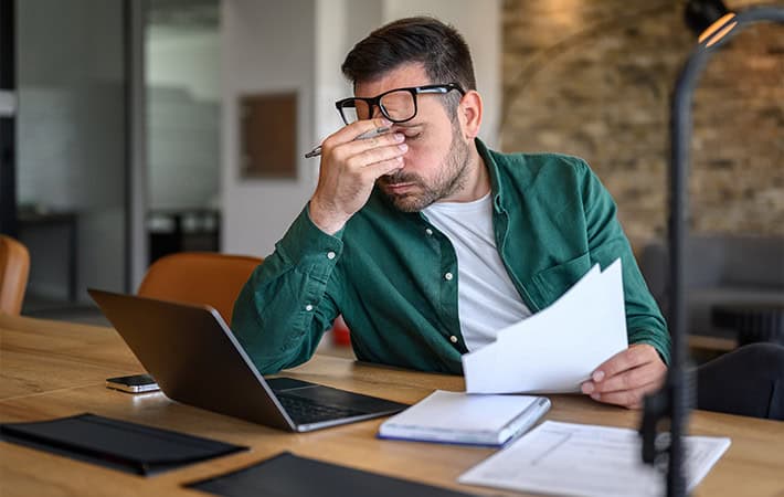 Stressed man reviewing paperwork at laptop desk