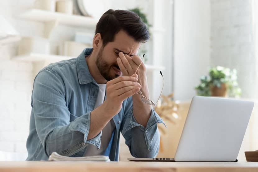 Tired man rubbing eyes beside laptop at home